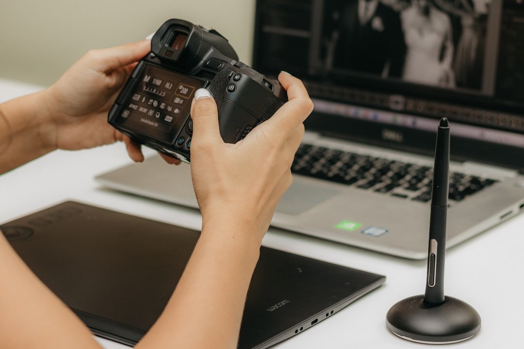 Close-up of hands editing photographs on a laptop next to a camera